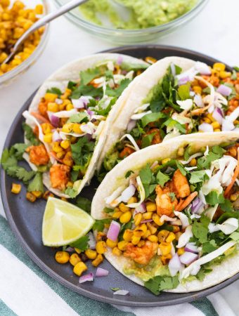 tacos on a plate with shrimp, corn and red onion.