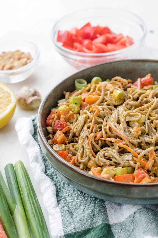 Soba noodle salad in a bowl with vegetables around it.