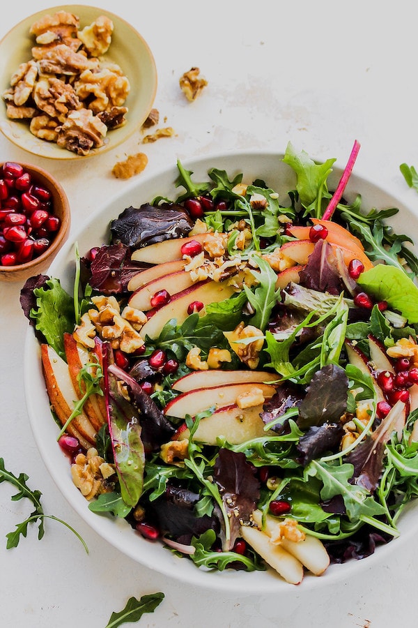 A bowl of lettuce with walnuts and apples.