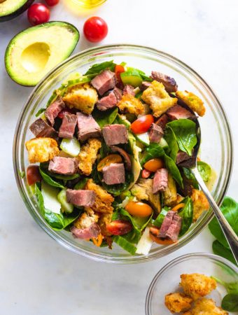 Steak salad in a bowl with food around it.