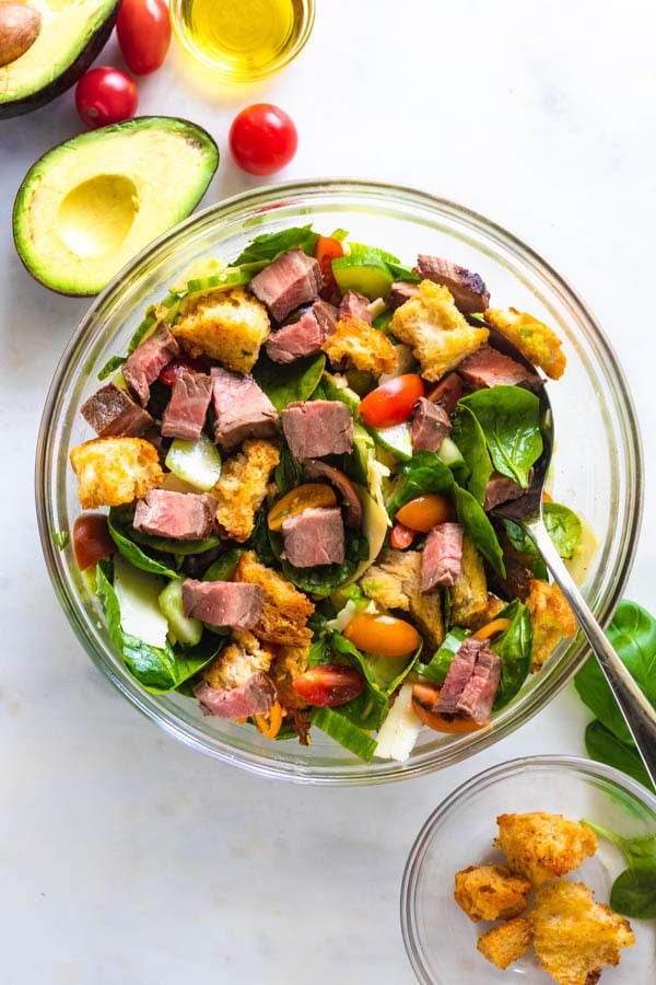 Steak salad in a bowl with food around it.