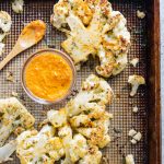 cauliflower steak on a sheet pan with spoon and red pepper sauce.