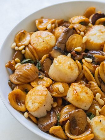 A side view of scallops with pine nuts sprinkled on top.