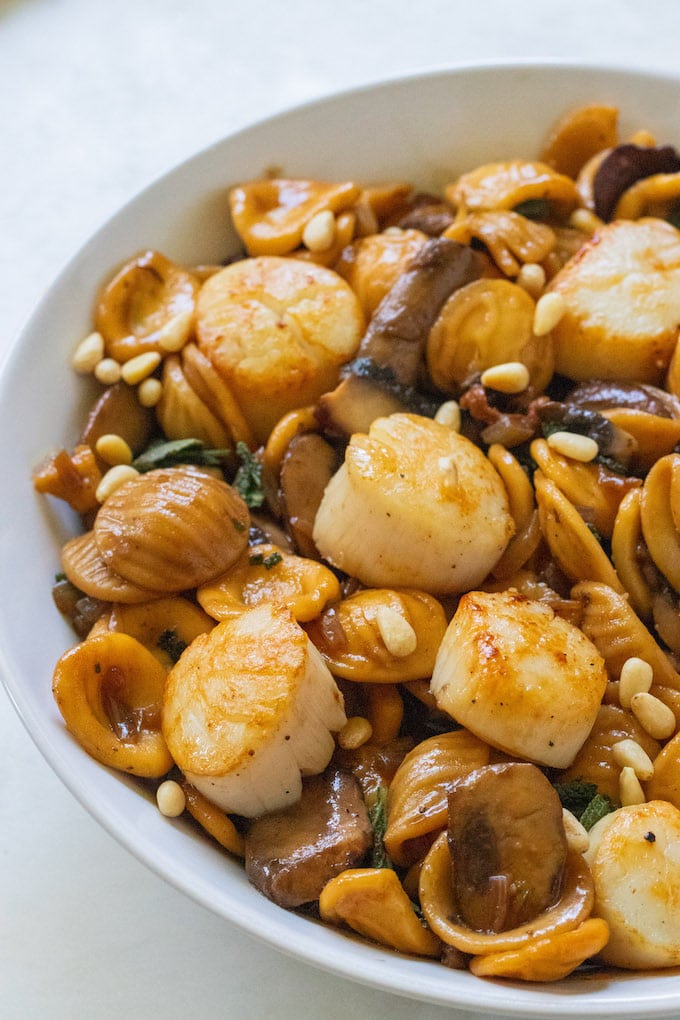 Scallops in a brown butter sage sauce with pine nuts on top.