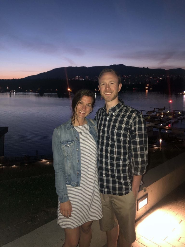 2 people standing on a dock in Vancouver at night with mountains in the background. 