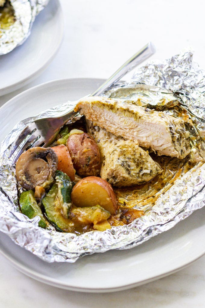 Cut chicken with vegetables in foil with a fork on a plate.