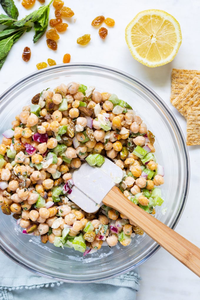 Chickpea salad with a spatula coming out of it with ingredients around it.