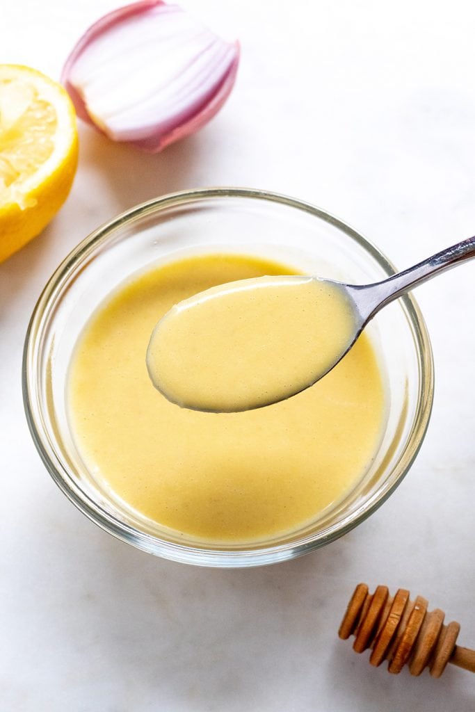 dressing in a bowl with a spoon and lemon next to it.