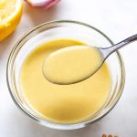 Creamy dressing in a bowl with a spoon and ingredients around it.