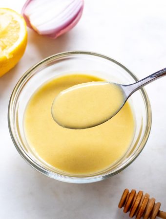 Creamy dressing in a bowl with a spoon and ingredients around it.