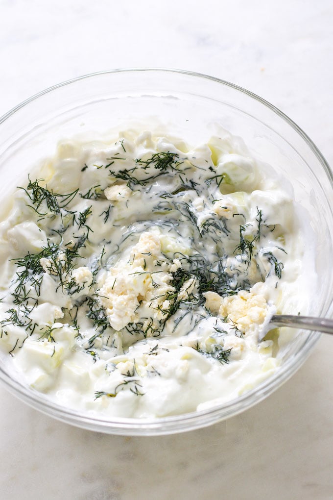 Feta, yogurt, dill, cucumber and lemon in a bowl being mixed. 