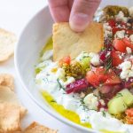 A bowl of cucumber dip with a chip being scooped into it.