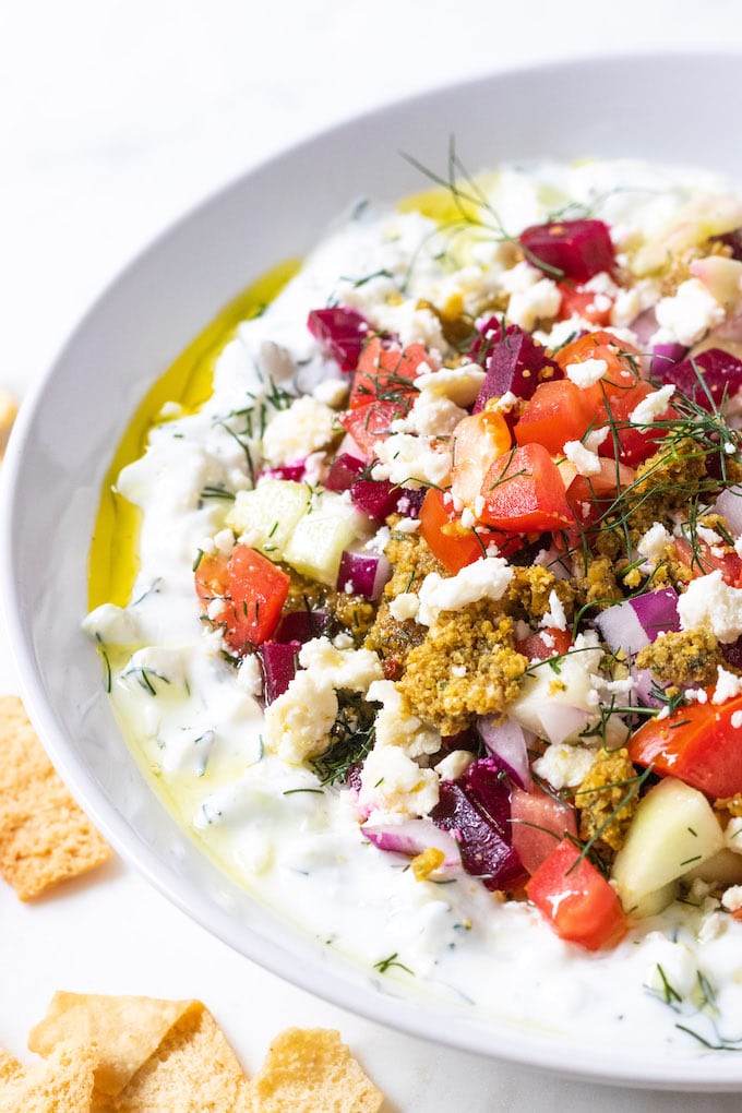 Mediterranean dip in a bowl with toppings and pita chips.