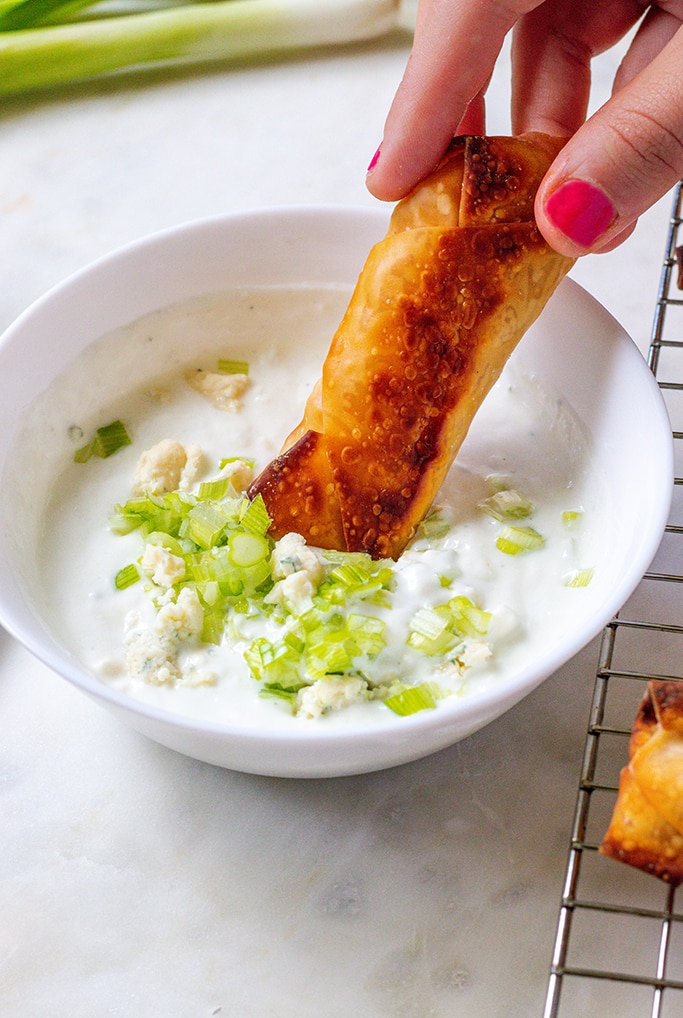 Up close shot of an wonton roll being dipped into blue cheese dip with green onions.