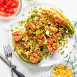 Grilled romaine salad on plate with chipotle shrimp and toppings on top.