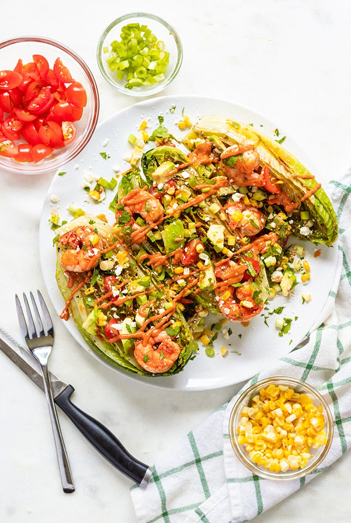 Grilled romaine salad with chipotle shrimp on a plate with toppings on it. 