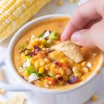 A chip being dunked in a bowl of corn chowder.