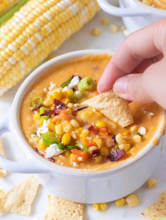 A chip being dunked in a bowl of corn chowder.