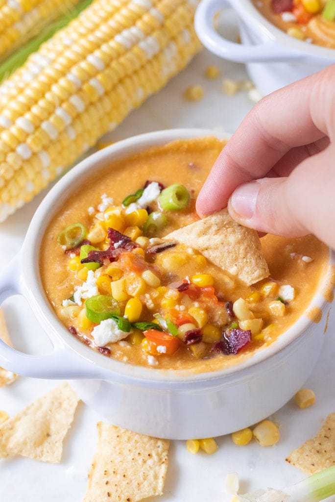 A chip being dunked in a bowl of corn chowder.
