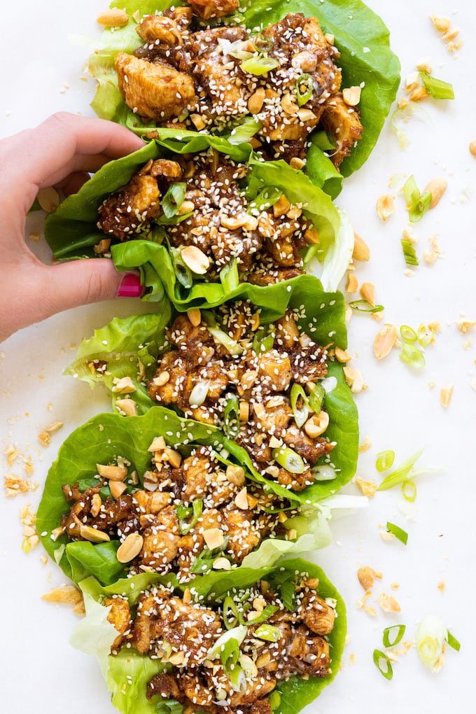 A hand grabbing a lettuce cup filled with chicken.