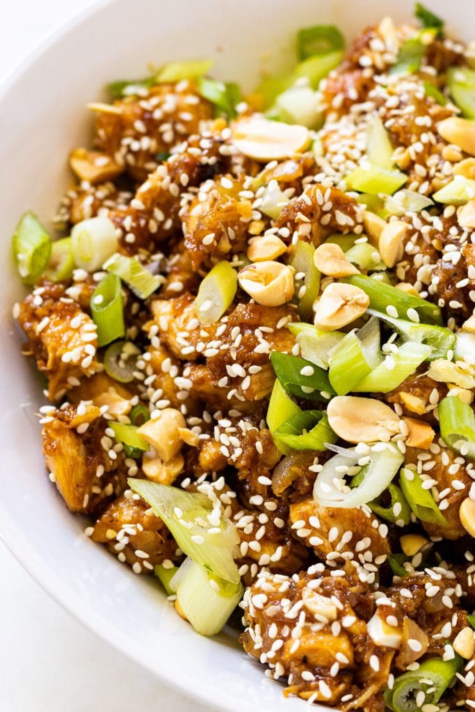 Scallions and peanuts on top of chicken and sesame seeds.