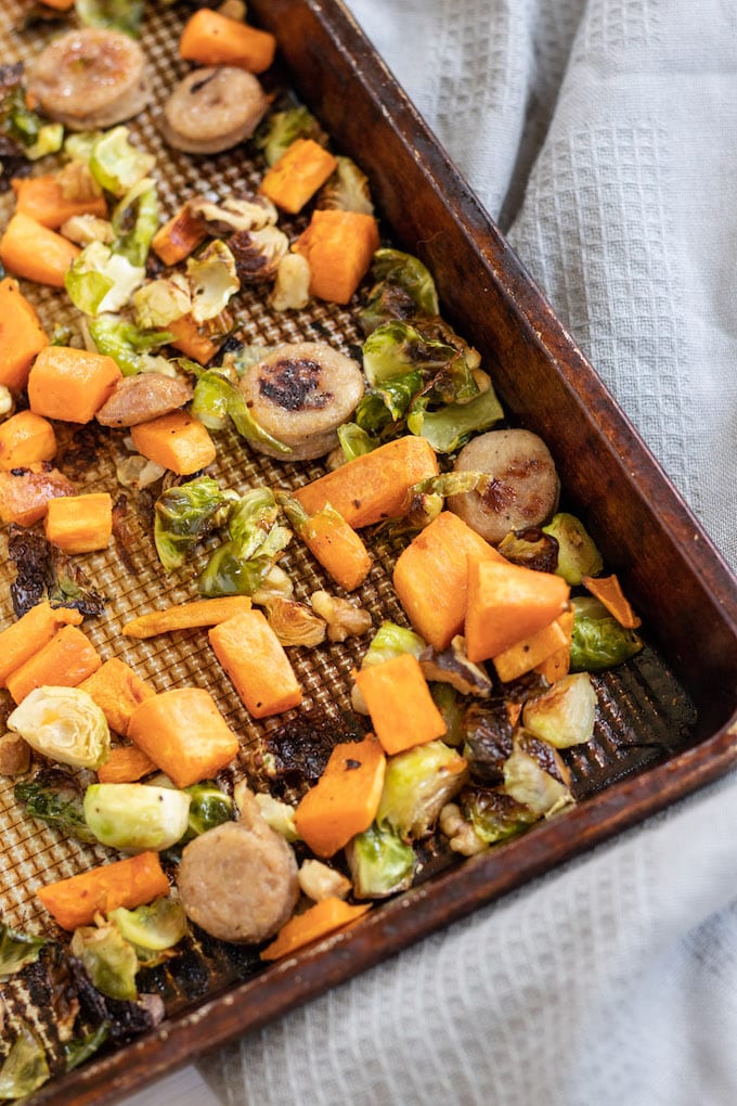 The corner of a sheet pan with vegetables and sausage in it.