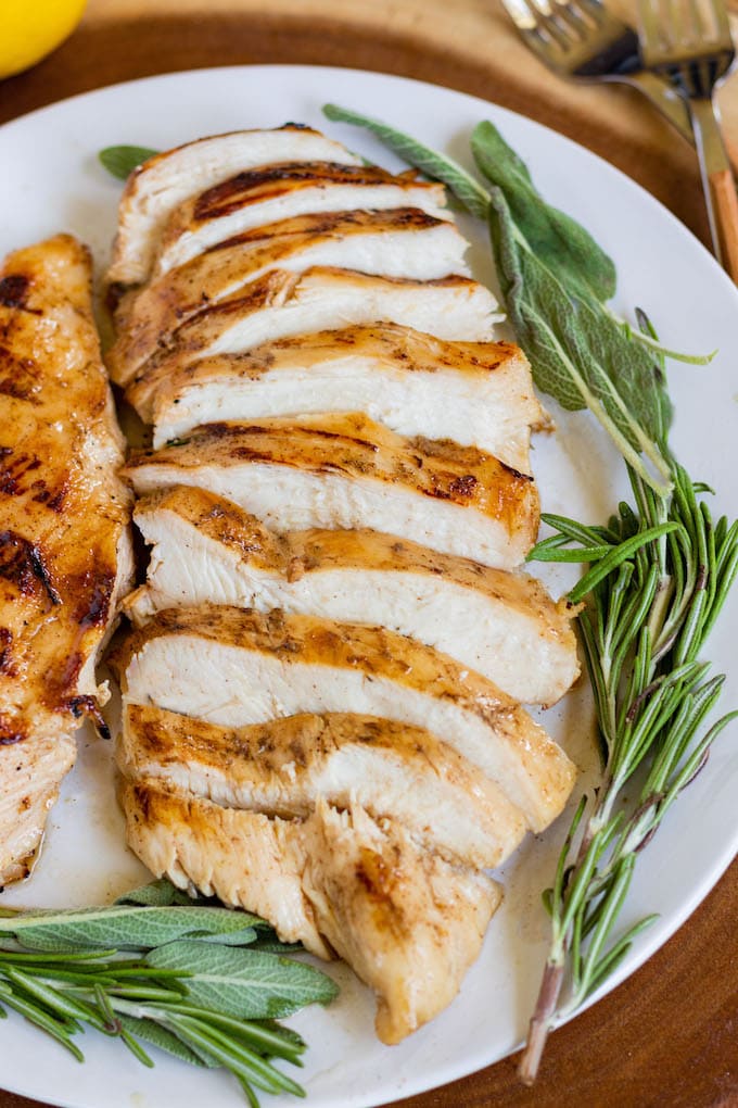 Cooked chicken on a plate with rosemary and sage.