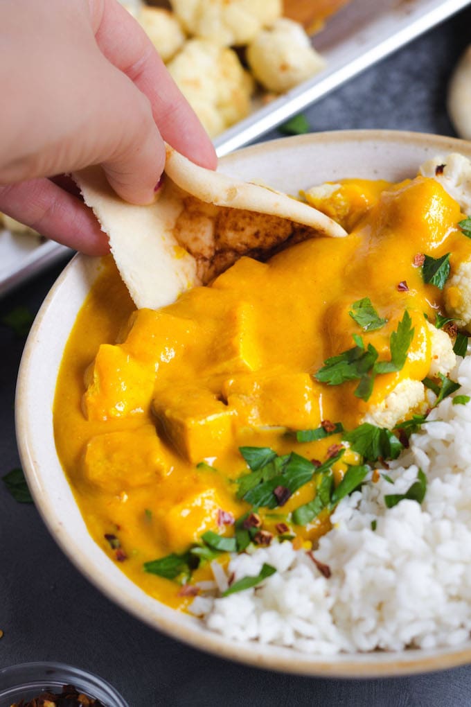 A hand dipping naan into butternut squash cauliflower curry.