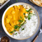 A bowl of butternut squash curry with toppings around it.