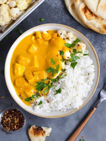 A bowl of butternut squash curry with toppings around it.