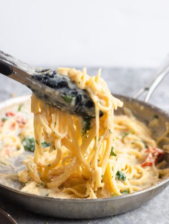 Tongs scooping up chicken Alfredo pasta.