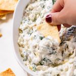 A chip dipped into a large bowl with spinach and artichoke dip.