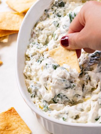 A chip dipped into a large bowl with spinach and artichoke dip.