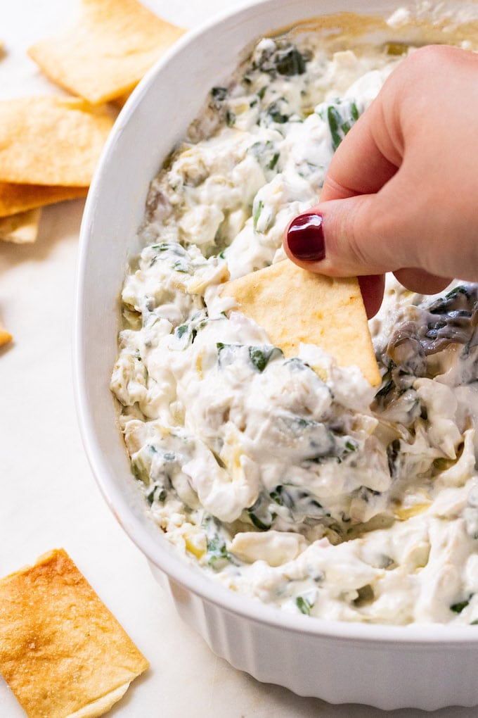 A chip dipped into a large bowl with spinach and artichoke dip.