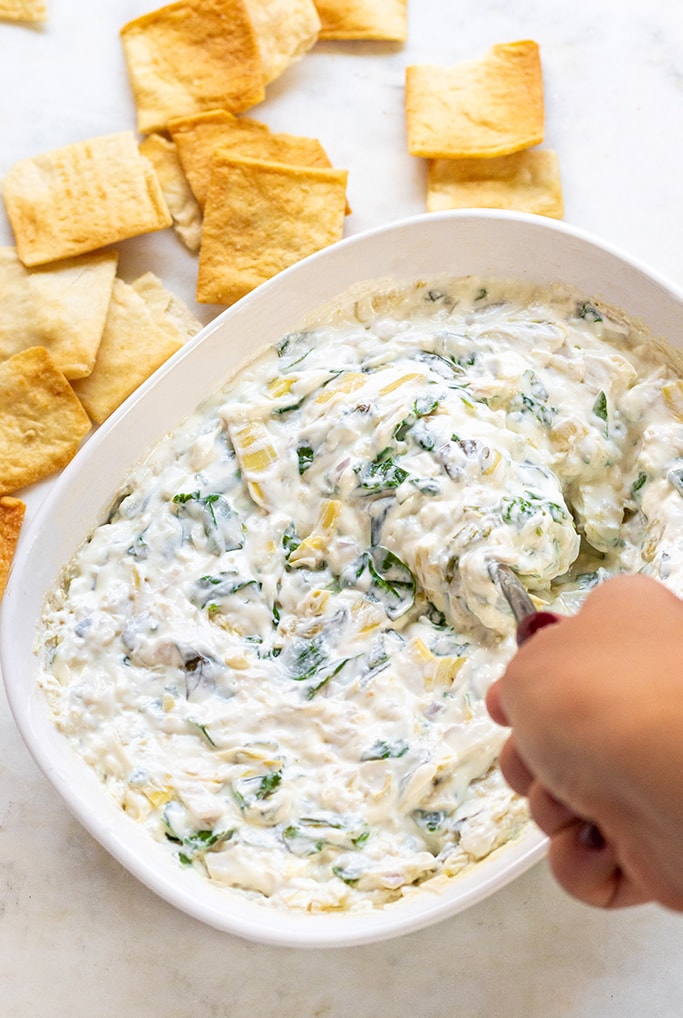 A bowl of spinach artichoke dip being stirred with a spoon.