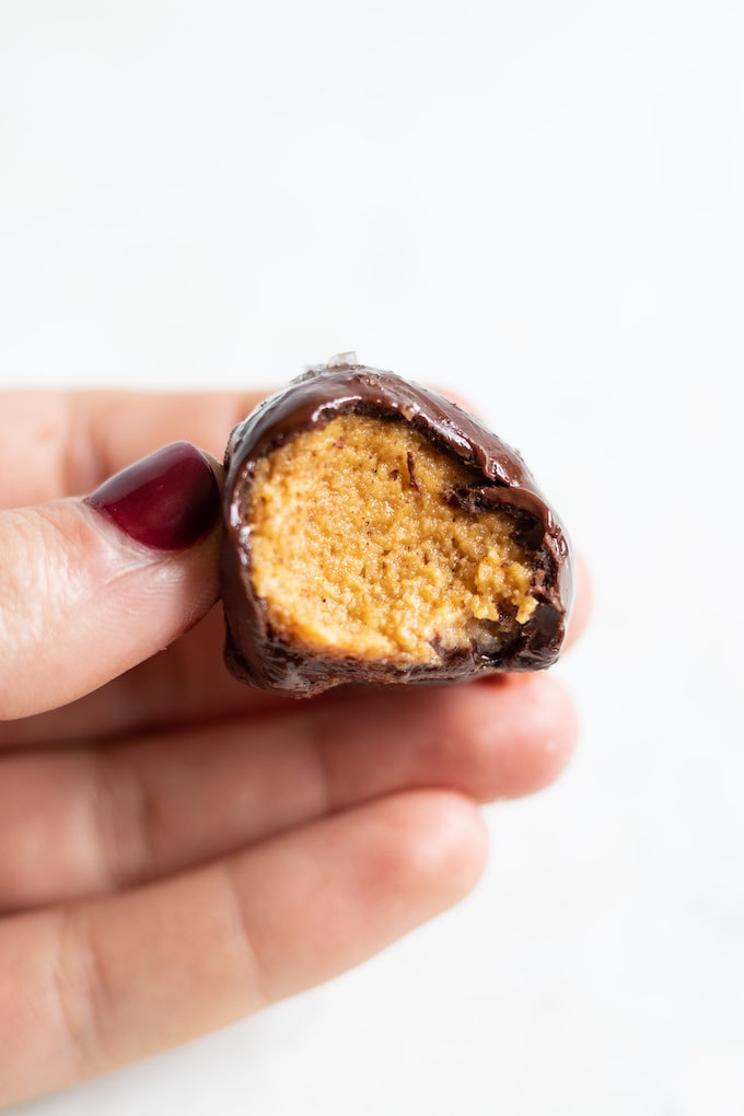 A hand holding a pumpkin pie truffle bite with a bite taken out of it.