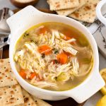 a bowl of lemon chicken orzo soup with crackers around it.