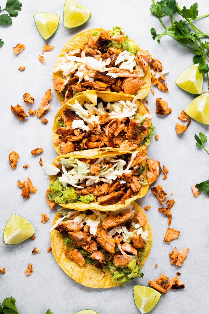 Tortillas lined up stuffed with blackened salmon and limes around it. 