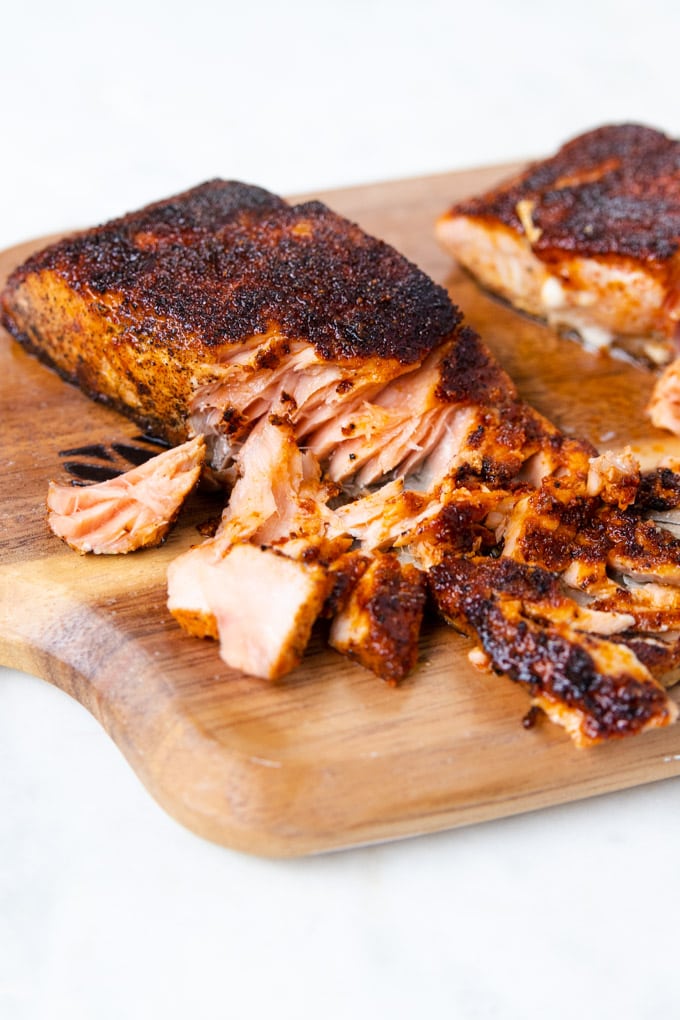 Blackened salmon filet flaked apart on a wooden plank. 