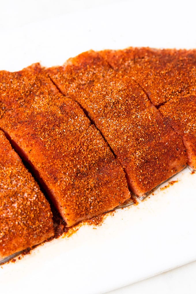 Raw salmon on a cutting board with seasoning. 