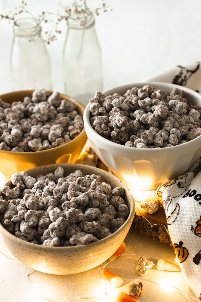 Three bowls of popcorn puppy chow with halloween items around it. 