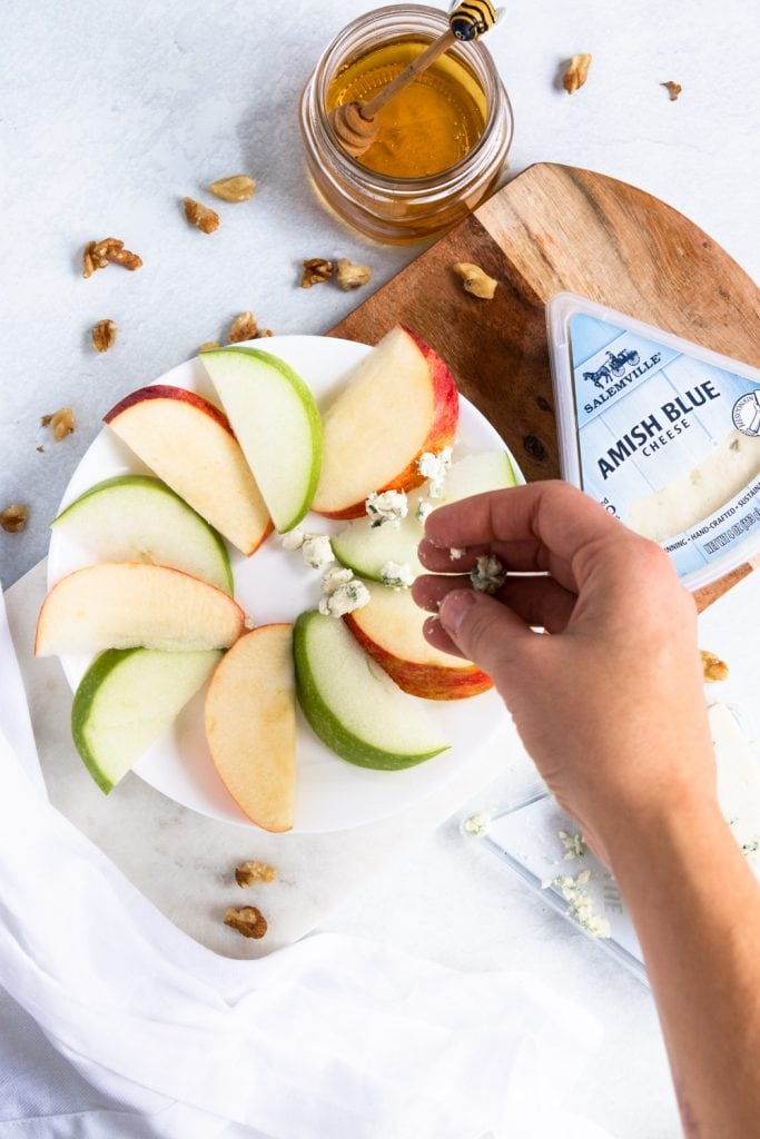 A hand sprinkling blue cheese on apples.