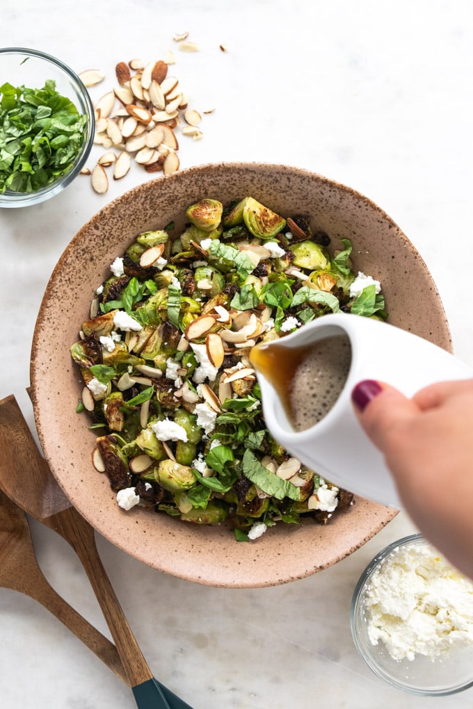 A hand pouring balsamic reduction onto brussel sprouts.