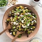 A bowl of brussel sprouts with wooden spoons and toppings.