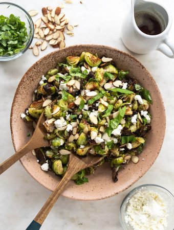 A bowl of brussel sprouts with wooden spoons and toppings.