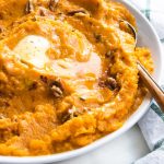 sweet potatoes in a bowl with butter and a spoon with pecans.