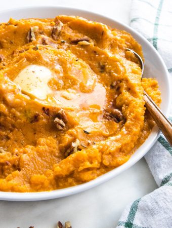 sweet potatoes in a bowl with butter and a spoon with pecans.