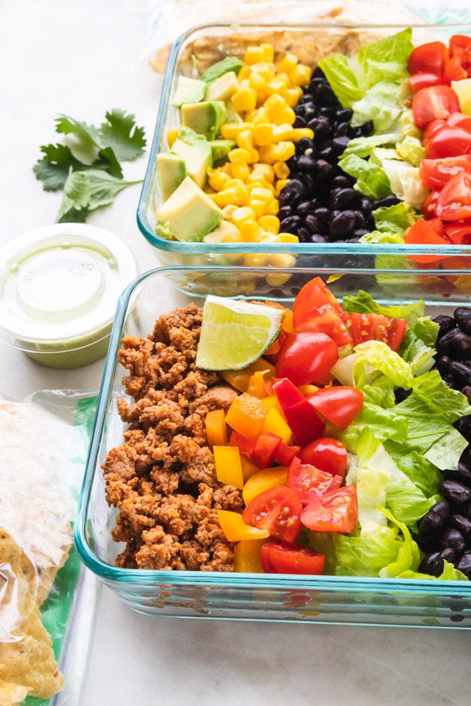 A side view of taco salad meal prep bowls with toppings on the side.