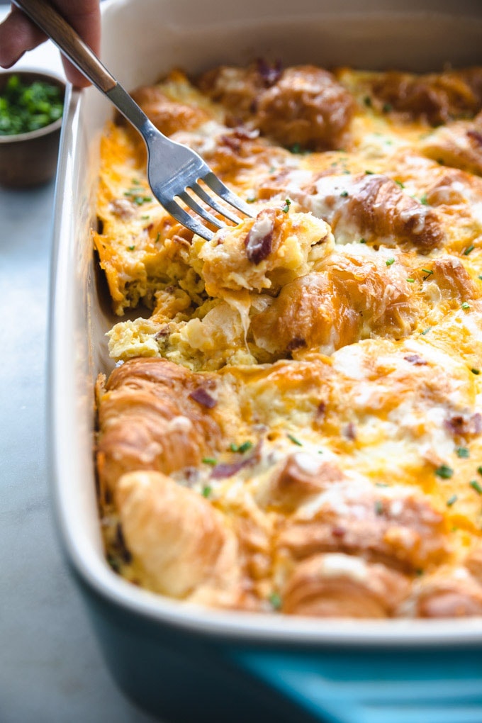 A fork with food on it over the breakfast strata with croissants dish.