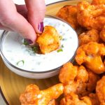 a hand dunking buffalo cauliflower into blue cheese sauce